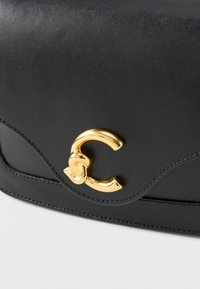 Borsa a tracolla in pelle nera con una texture liscia, caratterizzata da una chiusura dorata a forma di 'C' stilizzata e un design con pattina curva.