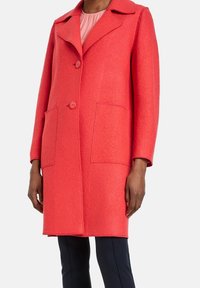 Coral wool coat with a structured collar, two front pockets, and front button closure. Features a soft texture and long sleeves.
