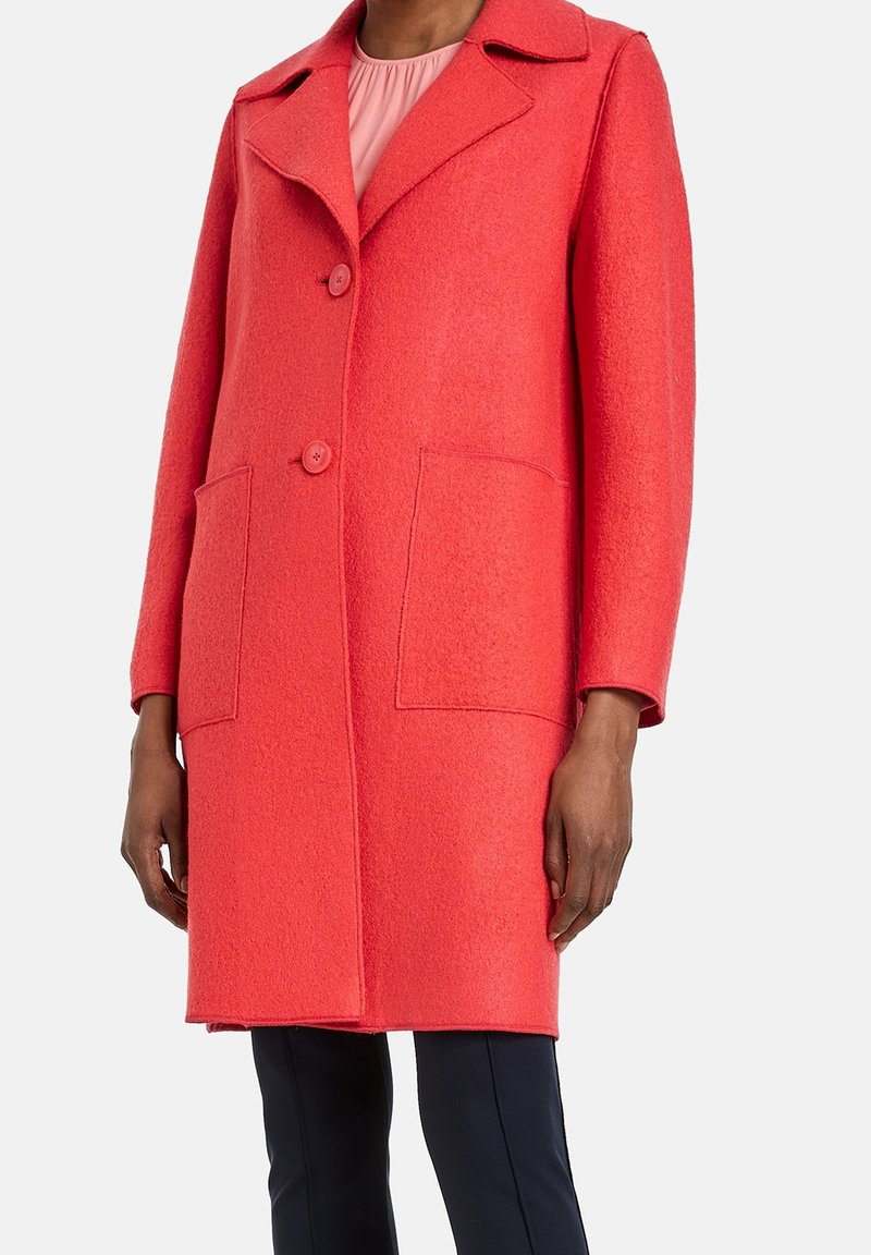 Abrigo de lana color coral con cuello estructurado, dos bolsillos delanteros y cierre frontal con botones. Presenta una textura suave y mangas largas.