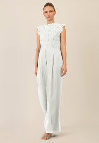 Mono blanco con bodice de encaje que presenta un escote con ondas y mangas cortas; pantalones de pierna ancha con pliegues frontales; tejido suave y ligero.