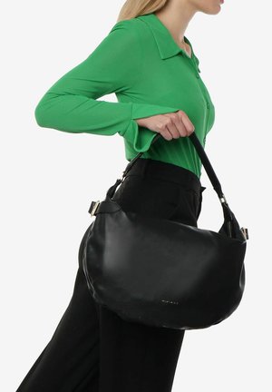Sac à main en cuir noir avec une texture lisse, grande forme arrondie et bandoulière réglable, tenu par une personne portant une chemise verte.