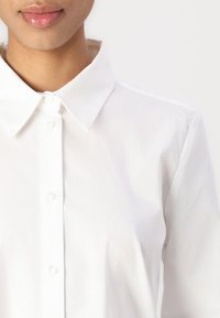 White button-up shirt featuring a classic collar, smooth texture, and subtle sheen. Buttons are positioned down the front.