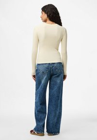 Ribbade ljuskrämfärgade långärmade toppar i kombination med högmidjade, lössittande blå denimjeans och avslappnade skor. Enkel, strukturerad design.