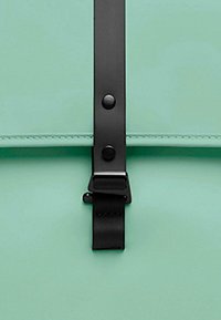 Mintgrønn ryggsekk med flatt design, utstyrt med en svart stropp og lås. Glatt tekstur med svarte metalldetaljer.