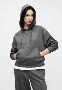 Γκρι φούτερ με κουκούλα, μπροστινή τσέπη, κορδόνια και ριμπ μανσέτες. Συνδυασμένο με γκρι παντελόνι που ταιριάζει και λευκό πουκάμισο από κάτω.