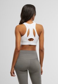 Hvit sports-BH med utskåret ryggdesign, sydd detaljer og en sikker passform. Kombinert med høyt liv grå tights.