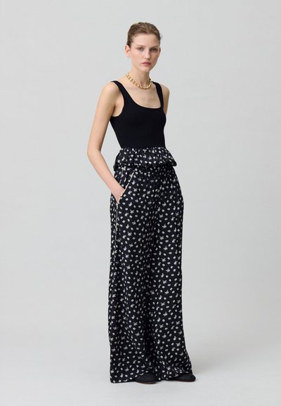 Top senza maniche nero abbinato a pantaloni larghi con motivo floreale. I pantaloni presentano una vita arricciata e tasche laterali.