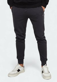 Dunkelgraue Sweatpants mit tailliertem Design, elastischem Bund und seitlichen Taschen, kombiniert mit weißen Turnschuhen mit schwarzen Akzenten.