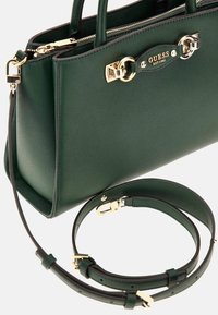 Borsa a tracolla verde con texture, hardware dorato, manici doppi e tracolla rimovibile. Presenta un'icona distintiva sul davanti.