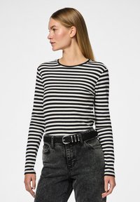 Camisa de mangas compridas com riscas pretas e brancas, com textura canelada e decote redondo, combinada com jeans pretos de cintura alta e um cinto.