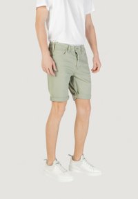 Shorts de mezclilla verde claro con dobladillos enrollados, con cremallera y cinco bolsillos, combinados con zapatillas blancas y una camiseta blanca.