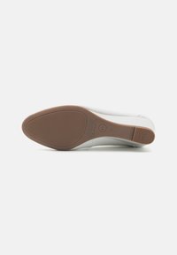 White, smooth shoe with a textured rubber sole, featuring a brown outsole and subtle branding. The design is minimalistic with no patterns.