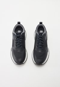 Zwarte sportieve schoenen met een bovenwerk van mesh, een gevoerde kraag en vetersluiting. Witte accenten op de buitenzool en logo-details aanwezig.