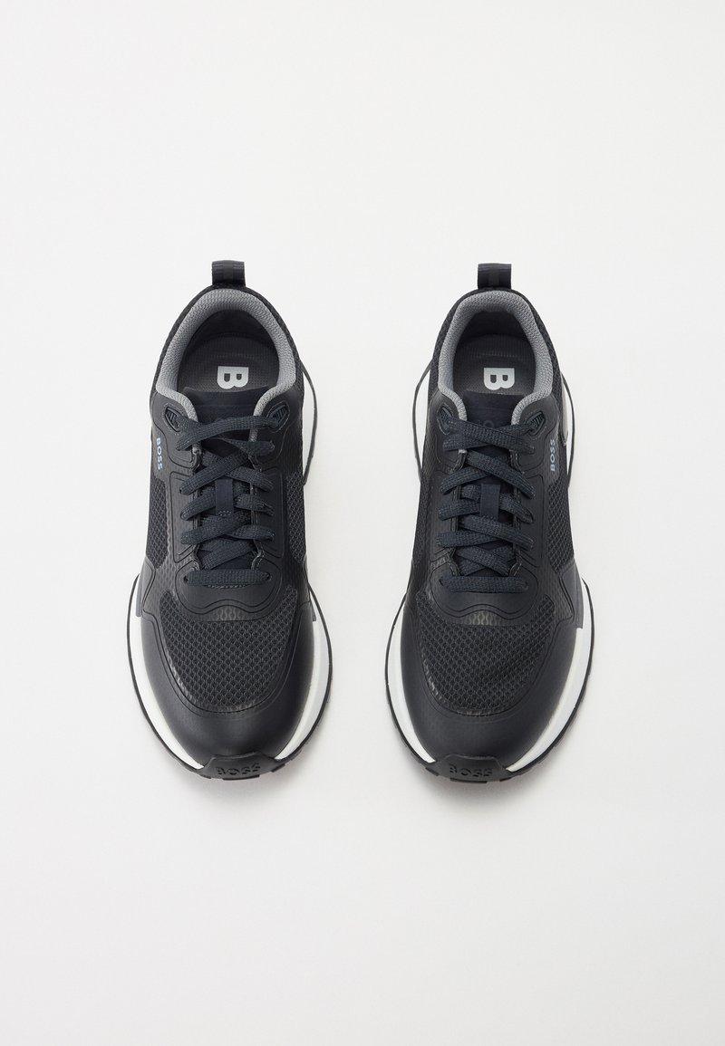 Schwarze Sportschuhe mit einem Obermaterial aus Mesh, gepolstertem Kragen und Schnürverschluss. Weiße Akzente an der Außensohle und ein Logo-Detail sind vorhanden.