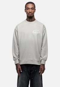 Lichtgrijze sweatshirt met ribgebreide manchetten en zoom, met een witte logo tekst op de borst. De stof lijkt zacht met een minimalistisch ontwerp.