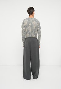 Cămașă cu mânecă lungă gri cu model de camuflaj, asociată cu pantaloni largi de culoare gri închis, cu dungi, care au două buzunare la spate și un centru elastic.