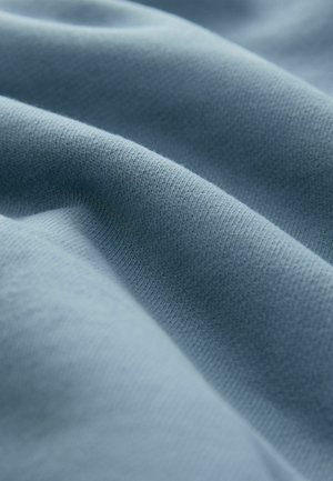 Weiches, strukturiertes Gewebe in Hellblau, das feine Strickmuster und sanfte Wellen zeigt und die biegsame und glatte Oberfläche betont.