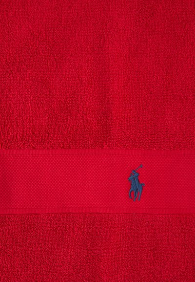 Κόκκινη πετσέτα με υφή και οριζόντια λεία λωρίδα με μικρό κεντημένο λογότυπο παίκτη πόλο σε ναυτικό μπλε.