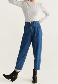 Hoge taille blauwe denim jeans met een losse pasvorm, voorzien van zijzakken en een knoopsluiting. Gekocht met een lichtgrijze textuurtrui en zwarte enkelboots.