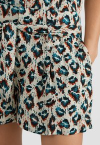 Béžové šortky z lehkého materiálu s barevným potiskem leopardího vzoru v tyrkysové, červené a černé; obsahují kapsy a odpovídající pásek.