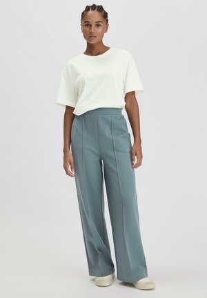 Lichtbeige, korte mouwen t-shirt gecombineerd met hoge taille, wijde teal broek. De stof is soepel, waardoor het een ontspannen pasvorm geeft.