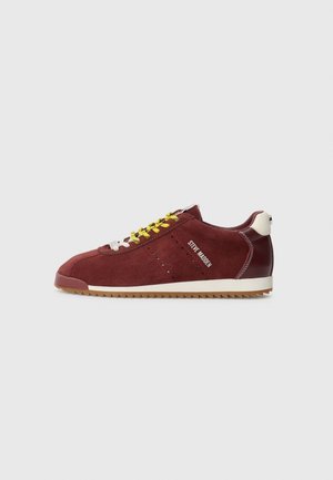Bordowe zamszowe buty sportowe z żółtymi sznurowadłami, białą podeszwą i brązowym bieżnikiem, z białym tekstem "Steve Madden" po bokach.