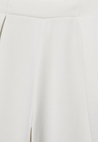 Jupe blanche taille haute avec plis et tissu lisse, montrant la partie médiane et la partie supérieure de la jupe en vue rapprochée.