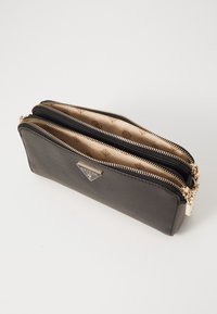 Schwarze Lederbörse mit zwei Reißverschlussfächern und einem goldfarbenen Logo-Akzent. Innenraum mit gemustertem Stoff ausgekleidet. Glatte Textur.