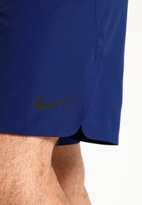 Shorts de sport bleu marine en matière synthétique, avec un logo Nike noir sur le côté et un ourlet courbé en bas.