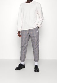 Long-sleeve cream shirt, checkered gray sweatpants with brown and black accents, and black shoes with white socks. Pants have tapered cuffs.