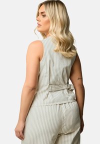 Ljust färgad ärmlös topp med vertikala marinblå ränder, har ett cinchrygg med ett knytband, tillverkad av mjukt, texturerat tyg.