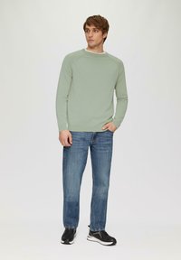 Hellgrüner gestrickter Pullover mit Rundhalsausschnitt, kombiniert mit ausgewaschenen blauen Jeans und schwarzen Sneakers. Lässige Passform, lange Ärmel.