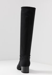 Botte noire jusqu'au genou en tissu extensible avec un talon bloc carré. Coutures le long des côtés. Texture lisse.