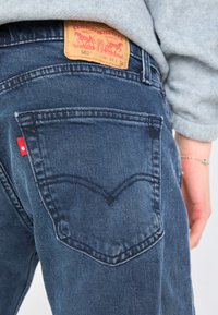 Levi's 502 džiny v tmavomodrom denime, s klasickým dizajnom na päť vreciek, červeným štítkom na zadnom vrecku a koženou nášivkou na páske.