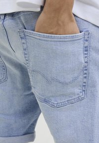 Ljust blå denimshorts med en synlig bakficka som har en enkel sydd design och uppvikta kanter. Slät textur och avslappnad passform.