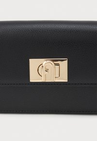 Primer plano de un bolso de cuero negro texturizado con un cierre de torsión rectangular dorado.