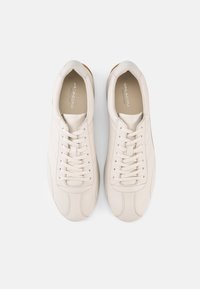 Λευκά δερμάτινα αθλητικά παπούτσια με ομαλή υφή, στρογγυλεμένη μύτη και δέσιμο με κορδόνια. Διαθέτουν διακριτικές ραφές και καφέ λαστιχένια σόλα.