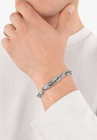 Pulsera de cadena de plata con un centro rectangular que presenta un diseño en mármol blanco y negro, llevada en una muñeca.