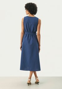 Blauwe mouwloze midi-jurk van textuurstof, met een ceintuur in de taille, een ruitpatroon en een rechte snit, afgewerkt met hoge sandalen.