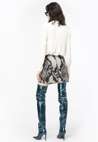 Vit blus med knäppningar vid ärmsluten, texturerad svart-vit orm-mönstrad kjol, högblanka teal stövlar med stiletto klackar upp till låren.