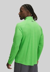 Groen sportshirt met lange mouwen, hoge kraag en een gemêleerde stof. Heeft een logo op de achterkant. Lichtgewicht en slim-fit ontwerp.