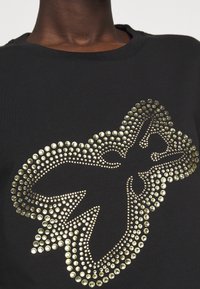 Sudadera negra con un diseño circular brillante y con tachuelas en dorado, con forma de mariposa, cuello acanalado y textura suave.