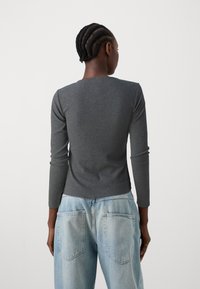 Haut à manches longues gris côtelé avec un col rond, associé à un jean baggy taille haute bleu clair avec deux poches arrière.