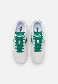 Hvite semskede sneakers med grønne detaljer og snøring, med en glatt overflate, rund form og logo på tungen.