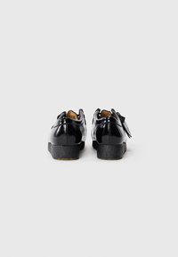 Black patent leather shoes with rounded toes and a textured black sole, featuring a decorative bow detail on the back.