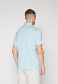 Lyseblå polo skjorte med krage, kort erme og siderifter i kanten. Stoffet har en teksturert overflate. Minimal merking på baksiden.