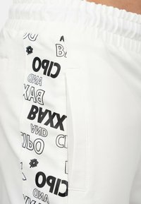 Pantaloni bianchi con pannello laterale e disegni testuali neri, tra cui "BAXX," "CIPO," e "AND" in vari caratteri. Vita elastica.