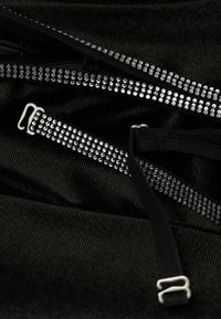 Tela negra con textura que presenta múltiples cremalleras adornadas con pequeños rhinestones plateados. Incluye correas negras planas y acentos de hardware metálico.