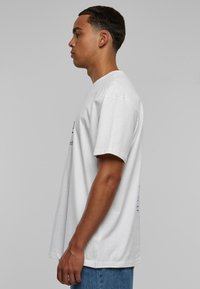 Hvid bomulds T-shirt med afslappet pasform, korte ærmer og rund hals. Viser grafik på forsiden og bagsiden i kontrasterende farver.