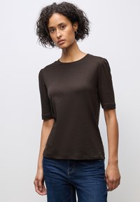 Bruine korte mouwen t-shirt van zachte stof, met een ronde hals en lichte pofdetails op de schouders, gecombineerd met blauwe jeans.